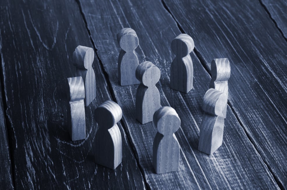 Wooden curly people stand in a circle around the person on a dark background. The concept of communication, teamwork, hierarchy and authoritarianism. Work team, relations and aggression.